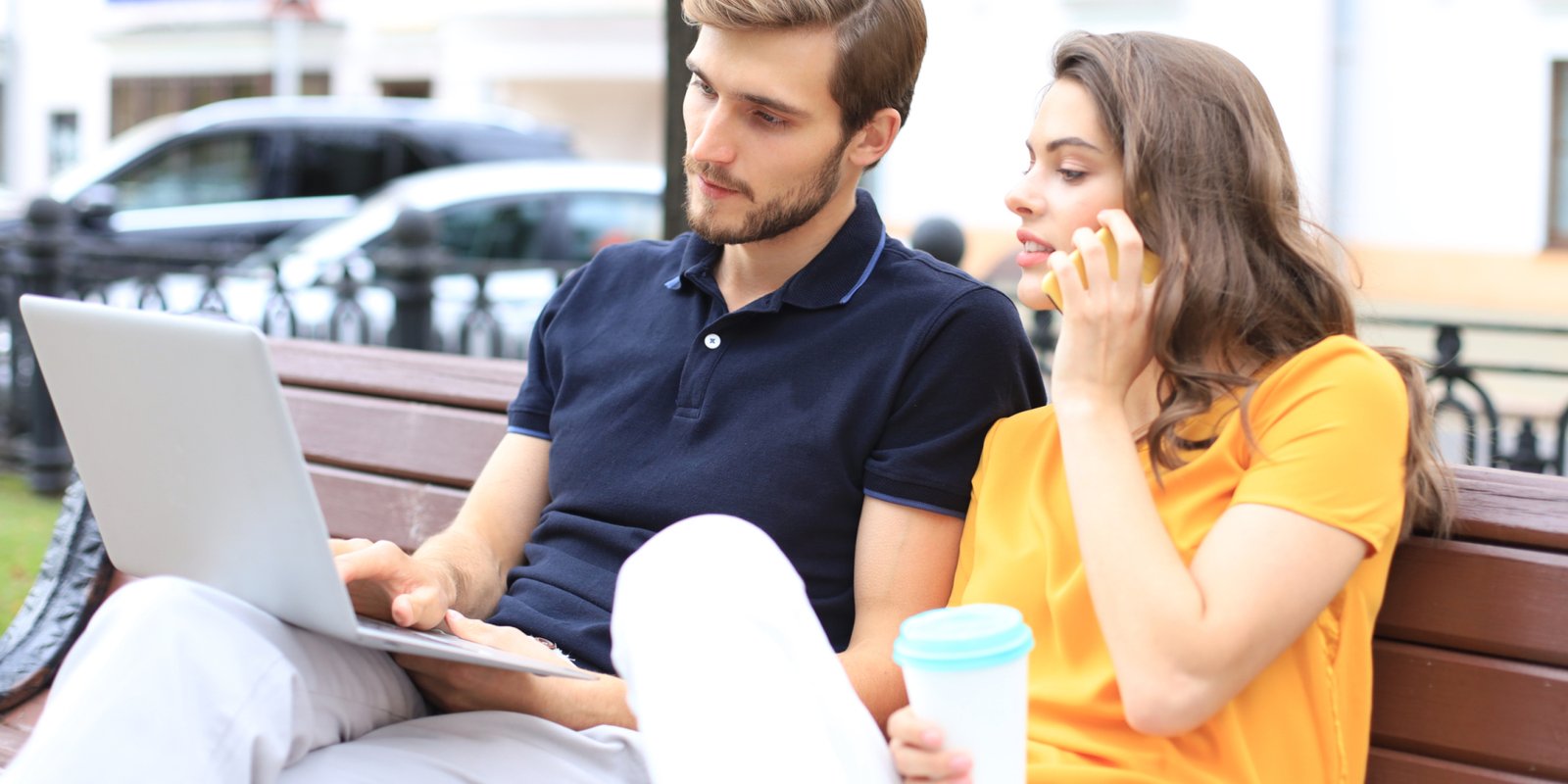 Attrative young couple using laptop computer while sitting on a bench outdoors