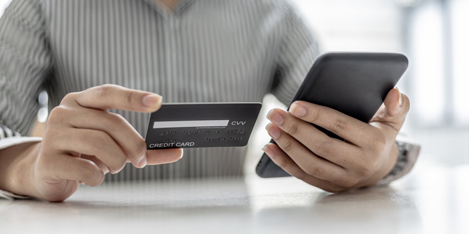 Woman holding a smartphone and a credit card, she is filling out her credit card information to pay for the purchases made through the smartphone app. Online shopping and credit card payment concept.